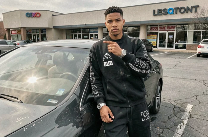 Jeune homme posant devant une voiture de luxe en location dans un parking banal, symbole des faux signes extérieurs de richesse